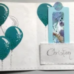 Biglietto di auguri fatto a mano per la Prima Comunione con tre palloncini nelle sfumature del blu e del turchese a sinistra, e i simboli dell'eucaristia (calice d'argento e ostia con scritta IHS) a destra su sfondo bianco materico.